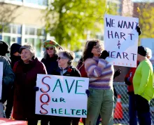 Protesters hold up signs supporting the Co-Operative Care Centre while traffic drives past the United Counties of Leeds and Grenville building on Tuesday morning, Nov. 4, 2025.